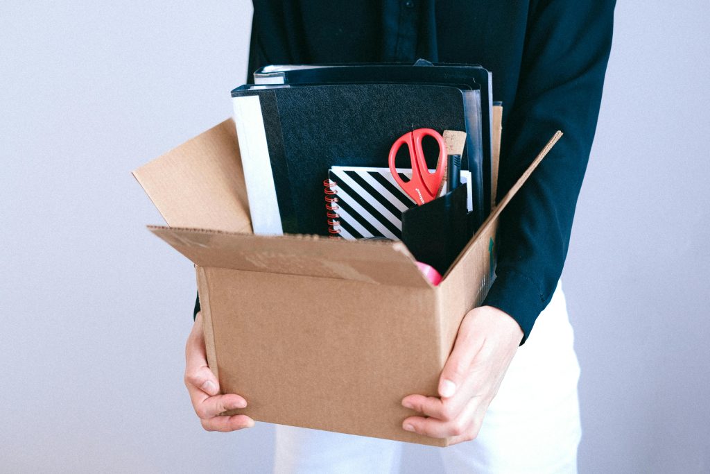 pexels-photo-4226206-4226206 Woman carrying cardboard box with office items like scissors and notebooks.